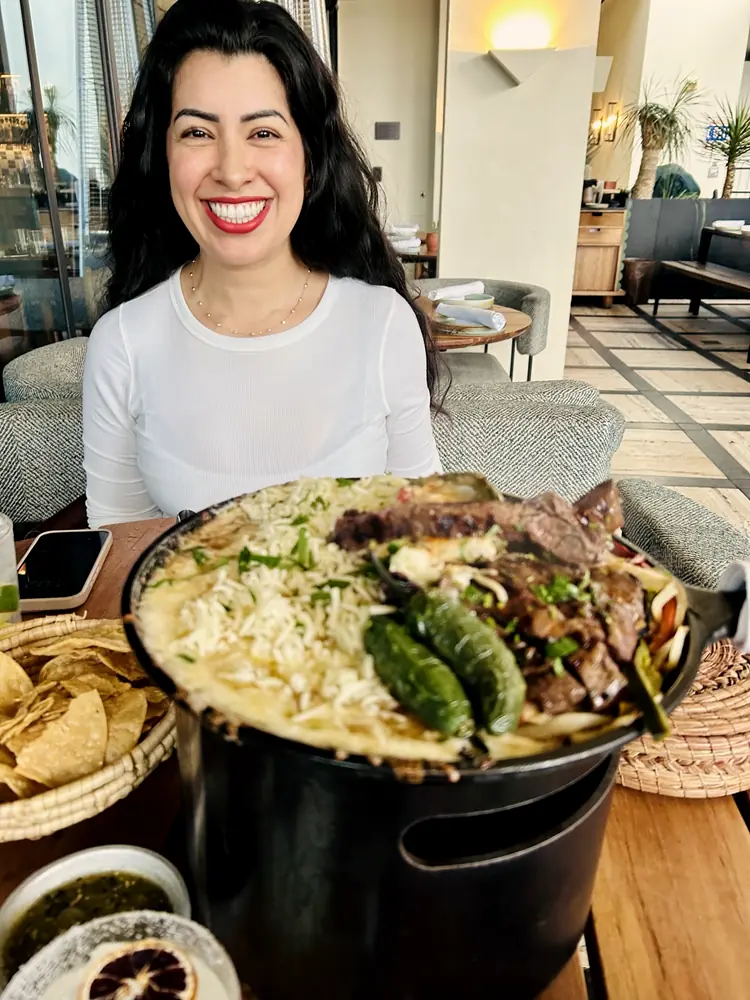 A woman smiling behind a generous shared dish at a gathering.