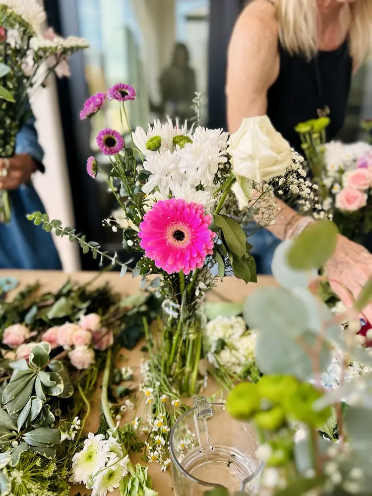 Hands arranging fresh flowers at a Becoming Beautifully gathering.