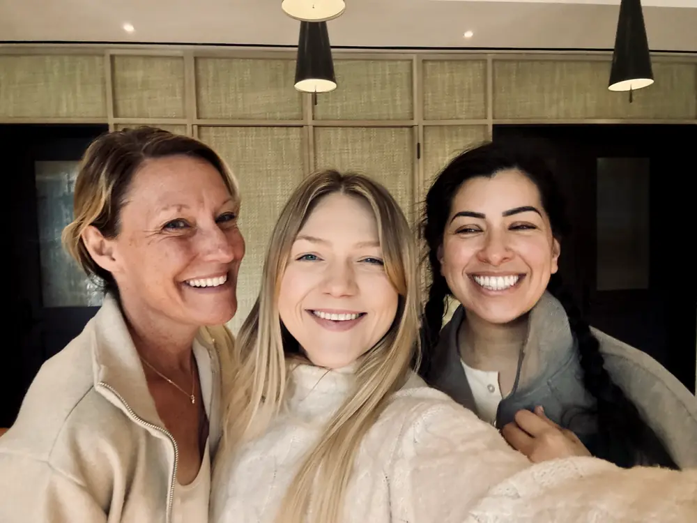 Three women smiling together at a gathering.