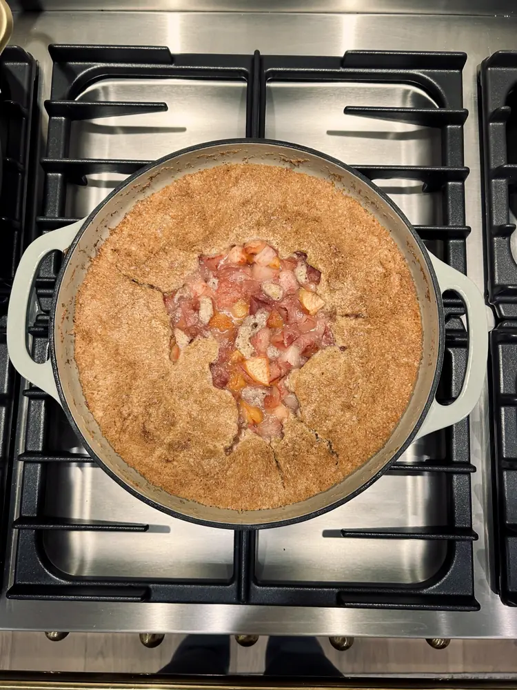 An overhead view of a fruit galette baking in a pot on the stovetop.