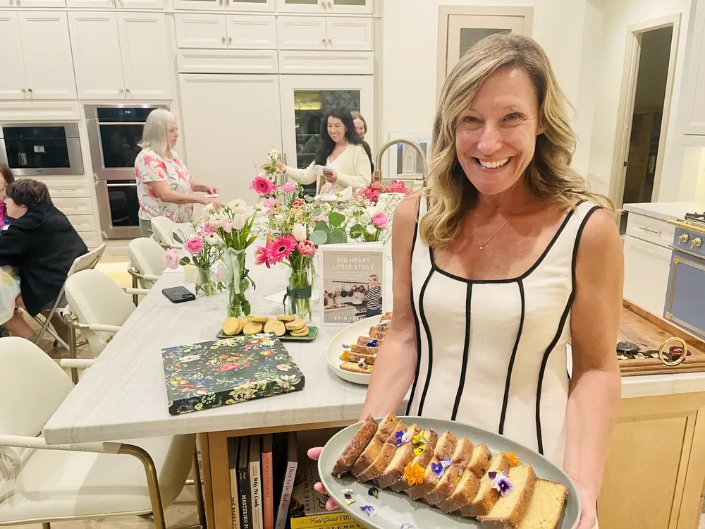 A host offering slices of fresh-baked cake beside flowers at a gathering.
